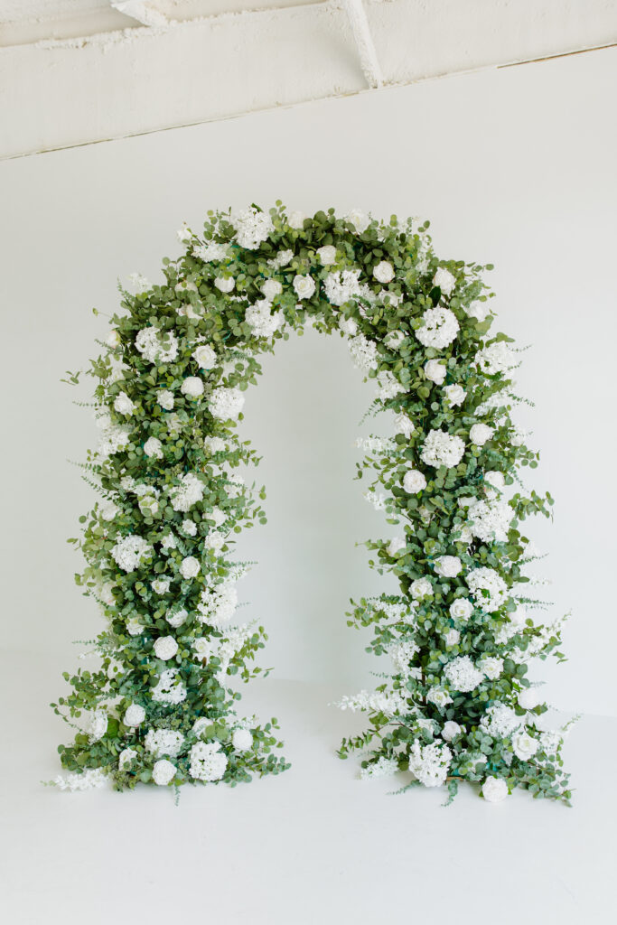 Green and white floral arch in front of a blank white wall by Lily and Olive