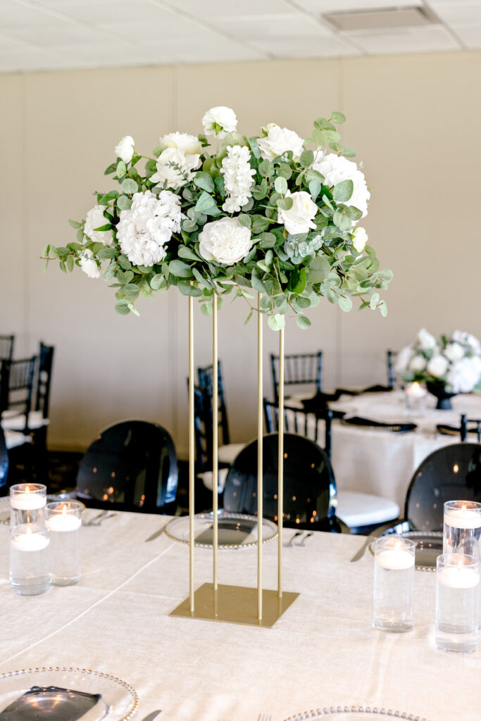 Wedding table floral arrangement in green and white foliage on a gold stand. 