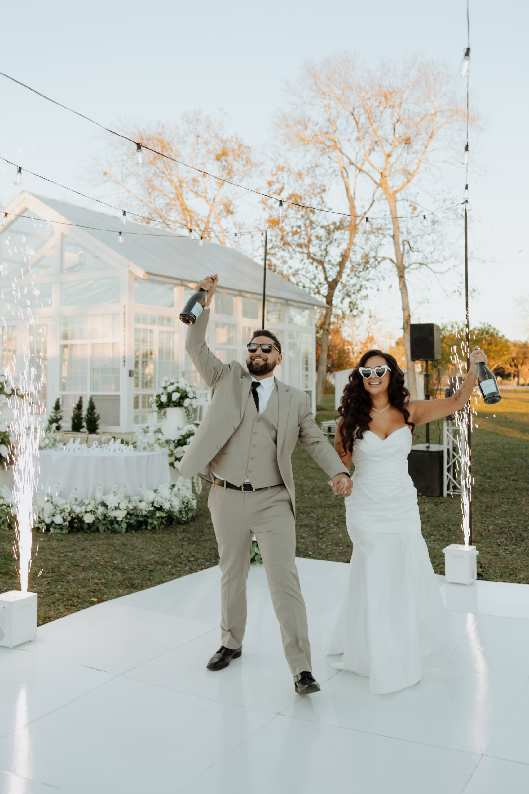 Bride and groom holding champagne bottles in front of The Makenzie House with cold sparks in the background